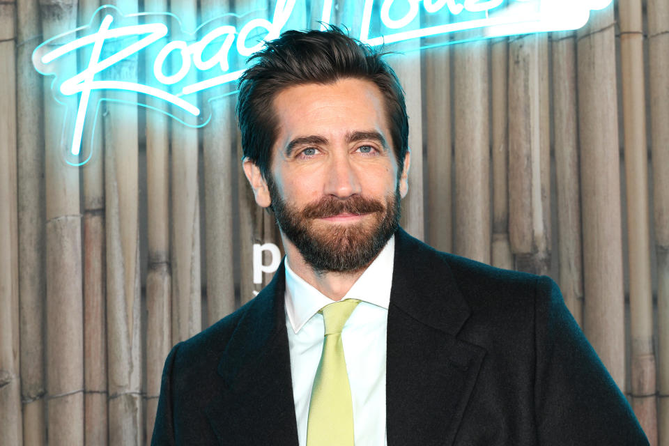 Jake Gyllenhaal in a classic suit, standing in front of a neon sign
