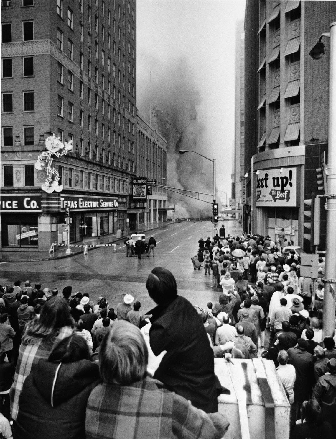 Implosion of the Worth Hotel seen by crowd from 7th Street at Burnett Park, Oct. 29, 1972. On the left there is a electric sign that reads “Texas Electric Service Co.” On the far right is an ad for “Mc Beef.”