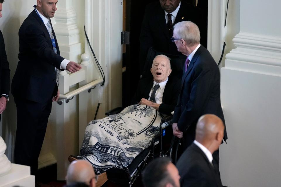 A photo of Jimmy Carter being escorted into a church for his wife's tribute service in a wheelchair.