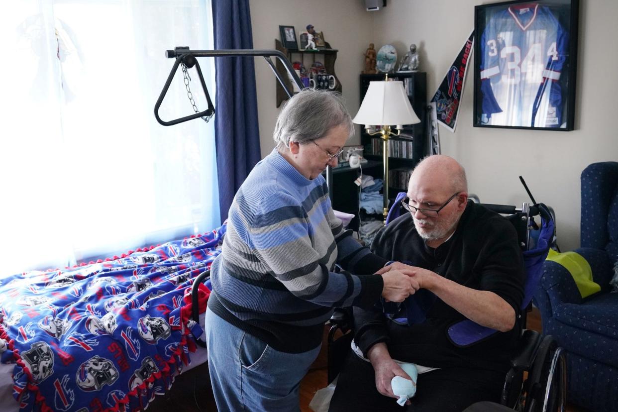 Teresa Brancato, who has been a caregiver for her husband, Joe, since he suffered a stroke in 2011, helps him clean up after lunch in the living room of their town of Tonawanda home.