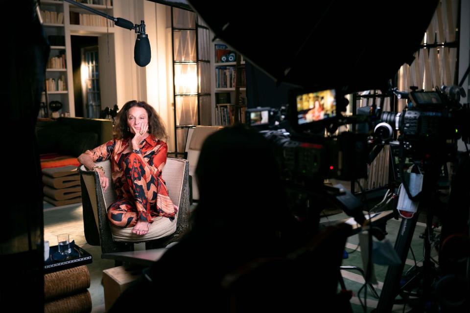 a brunette woman sitting on a couch with camera equipment around her