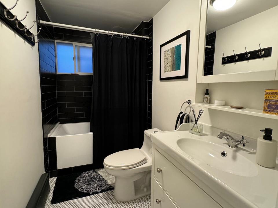 A bathroom with a black tiled tub and white toilet, sink, and anity with a diffuser and soap dispenser on top.