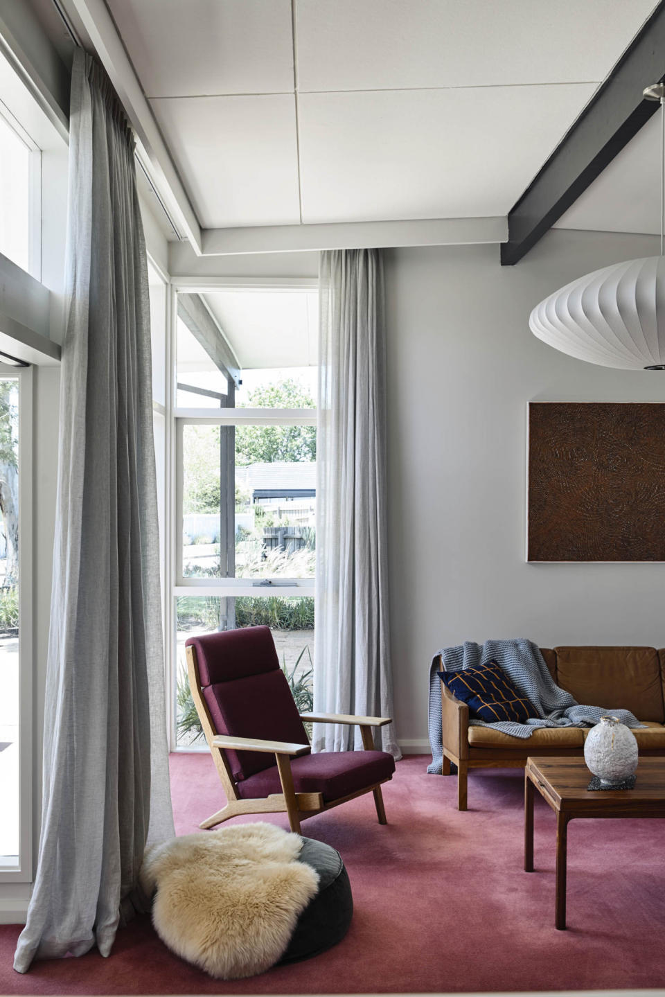 Living room with wine red carpet, light grey walls and curtains, dark wood furniture and deep blue cushion and throw