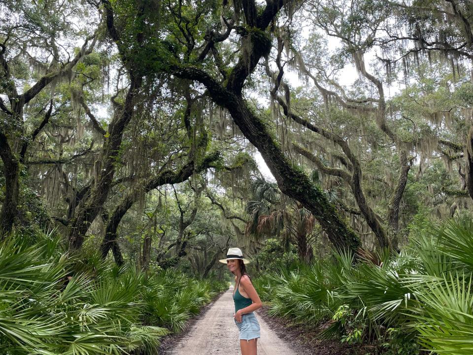 Emily standing on a path beneath massive, winding trees.