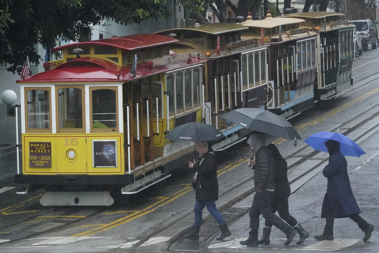 Pedestrians carrying umbrellas crossing in front of Cable Cars in San Francisco, Wednesday, Jan. 11, 2023. (AP Photo/Jeff Chiu)