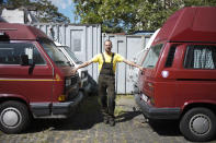 In this Tuesday, May 26, 2020 photo, Felix Rascher poses for a photo between Volkswagen camper vans he rent to tourists in a yard in Berlin, Germany. Germany's federal states are starting to reopen the touristic hotspots after the lockdown because of the coronavirus crisis and hope that German tourists will come. (AP Photo/Markus Schreiber)