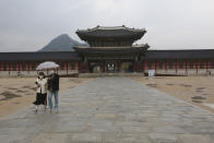 FILE - In this April 17, 2020 file photo, a couple wearing face masks to help protect against the spread of the new coronavirus walks in the rain at the Gyeongbok Palace, the main royal palace during the Joseon Dynasty, in Seoul, South Korea. Nervous travelers, spotty air service, health risks _ the battered global tourism industry is facing unprecedented uncertainty in the wake of the new coronavirus. Millions of workers are laid off or furloughed, and it will likely take years for the industry to get back to the strong demand it was seeing just six months ago. (AP Photo/Ahn Young-joon, File)