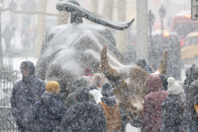 Pedestrians gather and take photos with the Charging Bull bronze statue near the New York Stock Exchange as snow falls accompanied by cold temperatures on Wall Street on Friday. Photo by John Angelillo/UPI