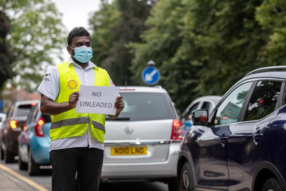 A Shell garage employee holds a sign on the side of the road informing a queue of traffic that they do not have unleaded petrol