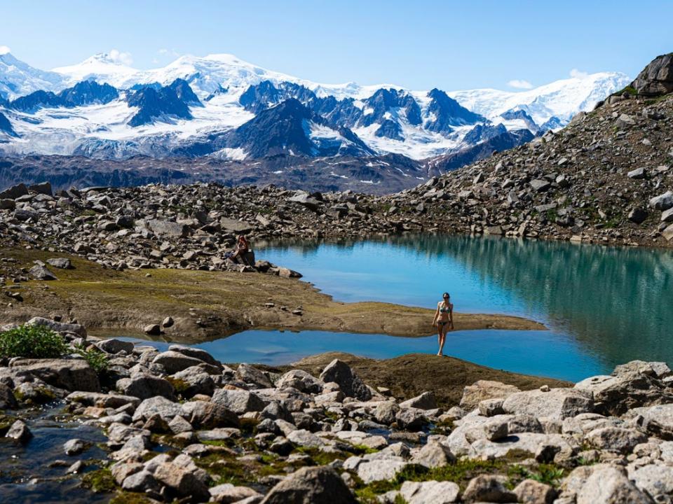 Woman standing by glacial pond in front of mountains and rocks in Alaska