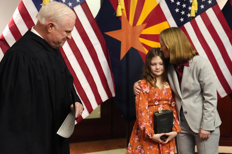 The new Arizona Attorney General Kris Mayes, right, a Democrat, kisses daughter Hattie, middle, after Mayes took the oath of office from Arizona Supreme Court Chief Justice Robert Brutinel, left, as, at the state Capitol in Phoenix, Monday, Jan. 2, 2023. (AP Photo/Ross D. Franklin, Pool)