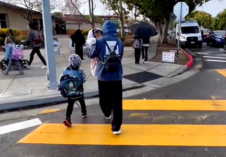 A parent walks with a baby and student to school on March 28, 2024.