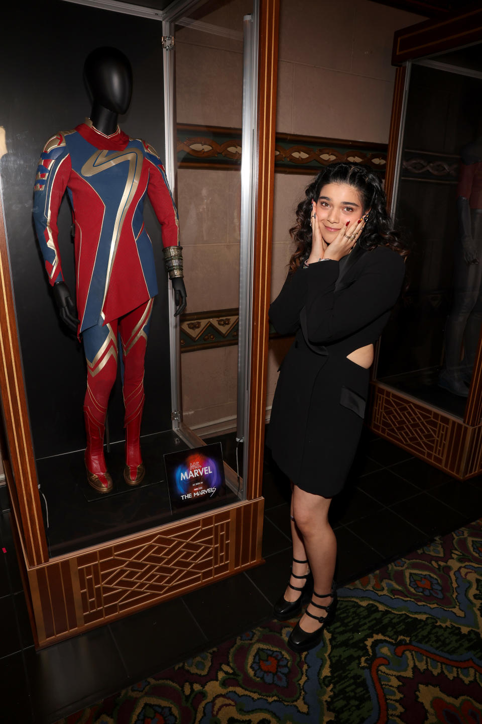 Iman Vellani standing next to an exhibit of her costume