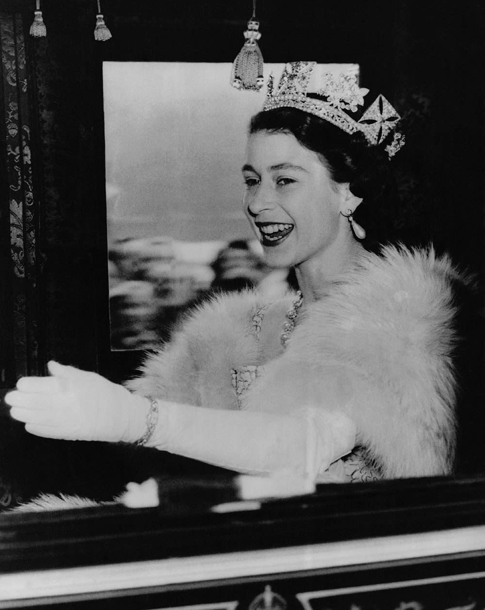 Queen Elizabeth smiling inside a royal carriage.