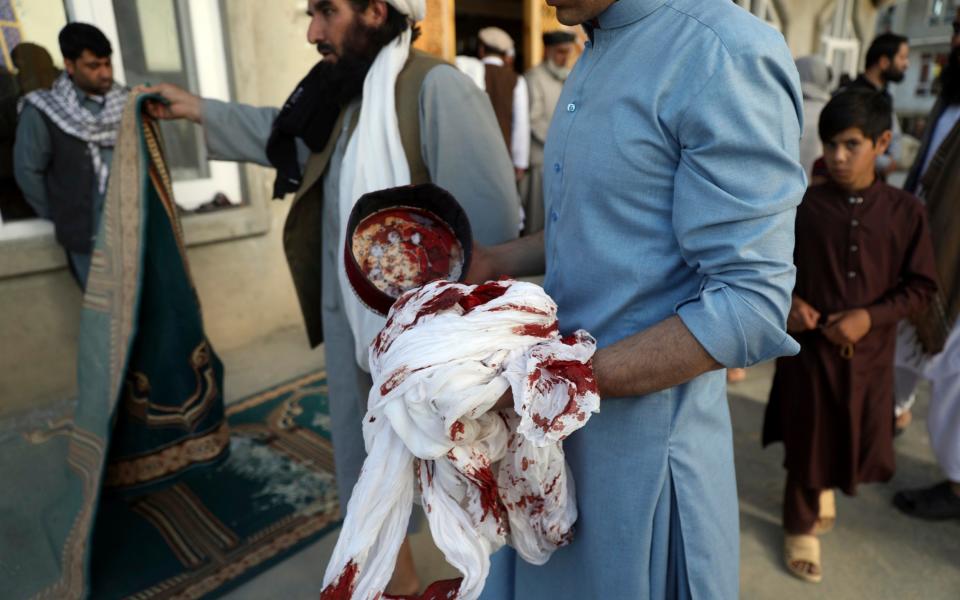 An Afghan man holds a blood-stained turban and cap found at the scene of the blast - Rahmat Gul /AP