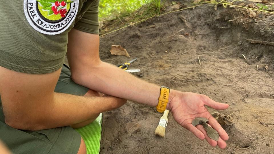 A researcher holds a silver fibulae, or brooch, at a dirt-covered excavation site.