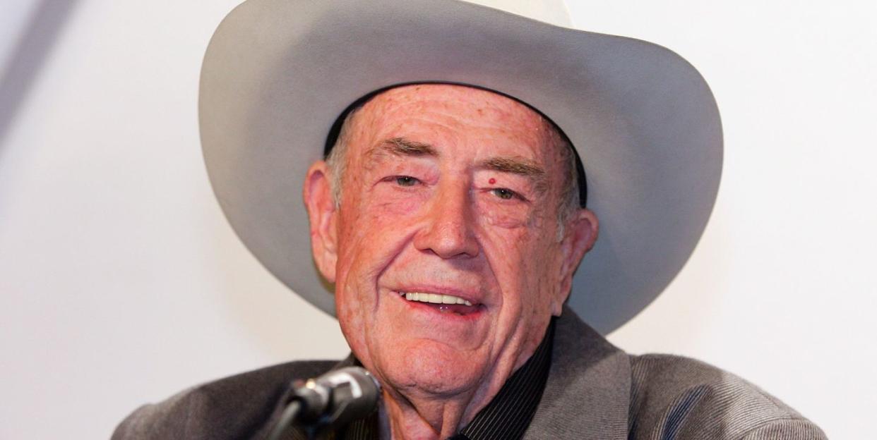 doyle brunson, wearing a gray suit jacket, black shirt, and white cowboy hat, talks into a microphone