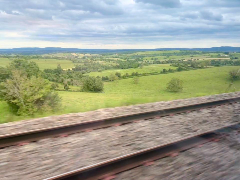 Undulating fields in France as viewed from a TGV, with a blurry railway track in the foreground