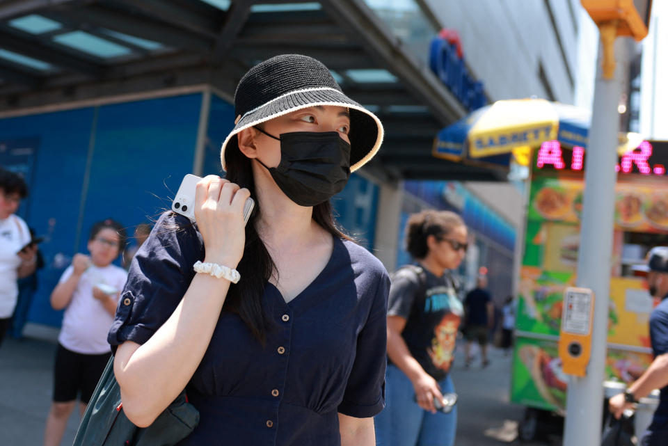 A woman wearing a hat and mask on a sidewalk.