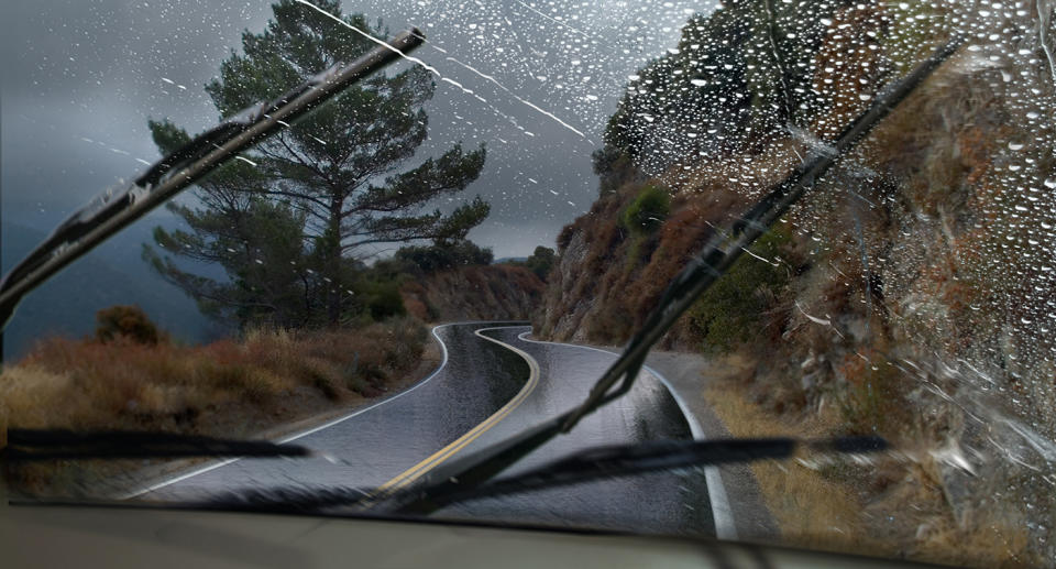 A vehicle driving through a rainy mountain road with the windshield wipers in motion.