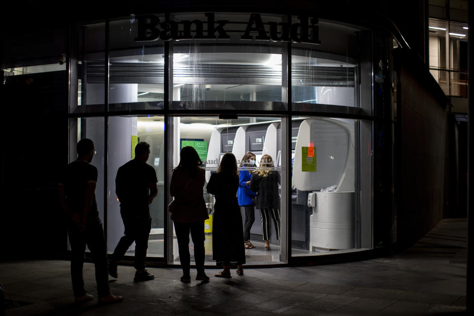 FILE - In this June 2, 2021, file photo, clients wait to use ATM machines outside a closed bank in Beirut, Lebanon. Lebanon’s local currency hit a new record low on Sunday, June 13, 2021, with the country's economic and political crisis worsening with no apparent solutions in the near future. (AP Photo/Hassan Ammar, File)