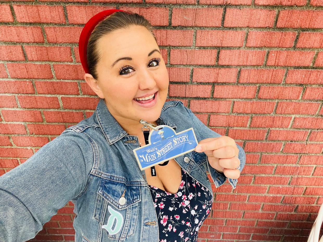 carly holding up her main street story lanyard and posing in front of a brick wall at disneyland