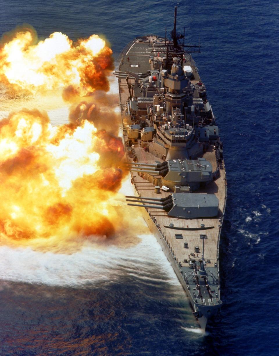 A bow view of the battleship USS Iowa firing its guns off the starboard side