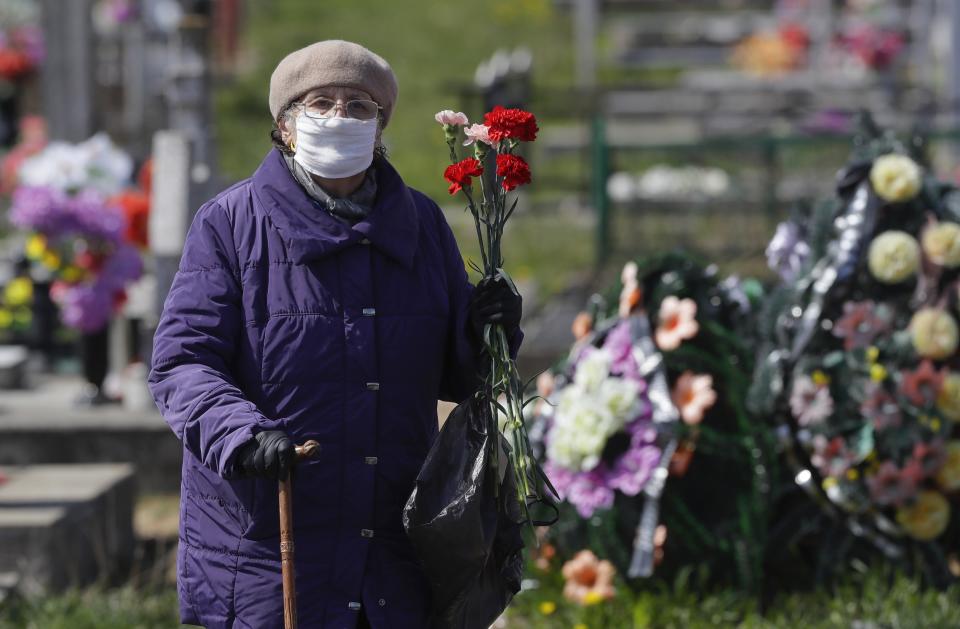 An elderly woman wearing a face mask to protect from coronavirus stands next the grave of her relative, during a traditional Orthodox Christian ceremony, in the town of Novogrudok, 150 km (93 miles) west of Minsk, Belarus, Tuesday, April 28, 2020. Tuesday marked celebrations of the church holiday "Radunitsa", a day of remembrance for the dead, on the ninth day after Orthodox Easter. Some people wear face masks to protect against COVID-19, although Belarus' president has dismissed concerns about the coronavirus despite a sharp rise in infections. (AP Photo/Sergei Grits)