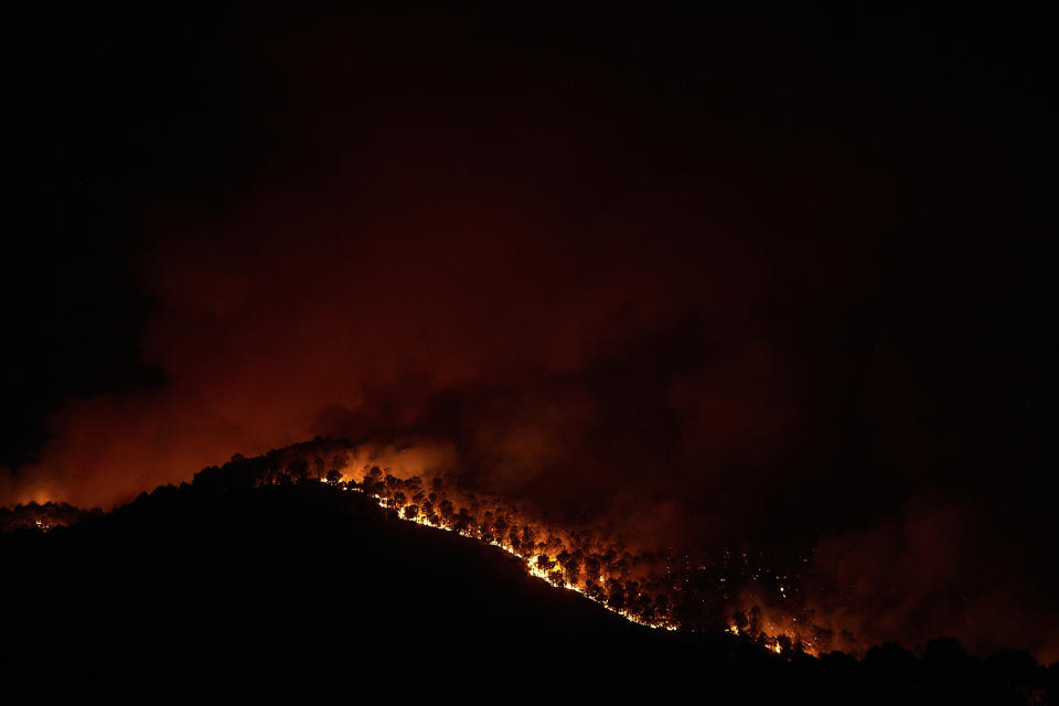 Trees burn as flames and smoke engulf the top of a hill in a forest fire in Artazu, northern Spain in the early hours of Sunday, June 19, 2022. Firefighters in Spain are struggling to contain wildfires in several parts of the country suffering an unusual heat wave for this time of the year. (AP Photo/Miguel Oses)