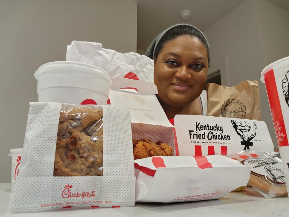 The writer smiles out from behind bags of chicken, cups, and other takeout from KFC and Chick-fil-A