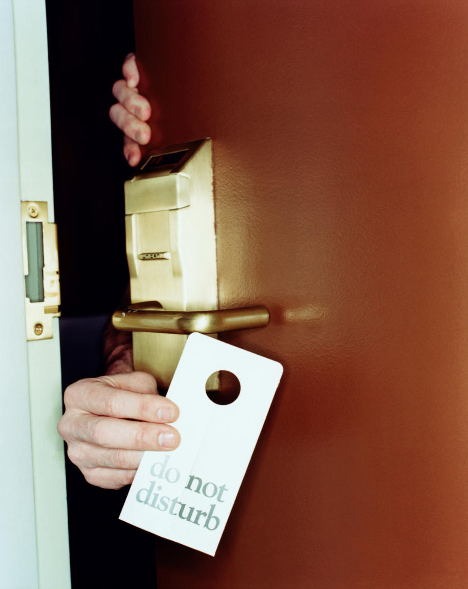 Person's hand holding a "do not disturb" sign while partially opening a hotel room door