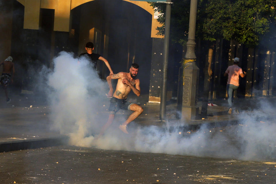 Anti-government protesters run amid tear gas fired by riot police during a protest marking the first anniversary of the massive blast at Beirut's port, near Parliament Square, In Beirut, Lebanon, Wednesday, Aug. 4, 2021. United in grief and anger, families of the victims and other Lebanese came out into the streets of Beirut on Wednesday to demand accountability as banks, businesses and government offices shuttered to mark one year since the horrific explosion. (AP Photo/Bilal Hussein)