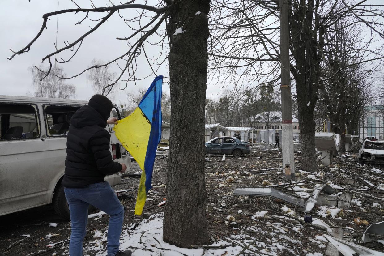 A man takes a Ukrainian national flag swinging from a tree as he walks near a destroyed accommodation building by a checkpoint in Brovary, outside Kyiv, Ukraine, Tuesday, March 1, 2022.