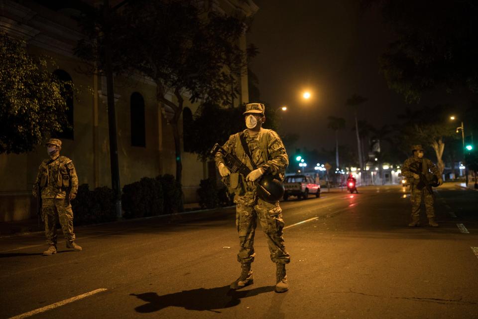 Soldiers wearing protective face masks as a precaution against the spread of the new coronavirus, stand guard at a check point minutes before the start of a curfew decreed by the government in Lima, Peru, Friday, March 20, 2020. Peru is in its fifth day of a government decreed state of emergency amid the presence of COVID-19.