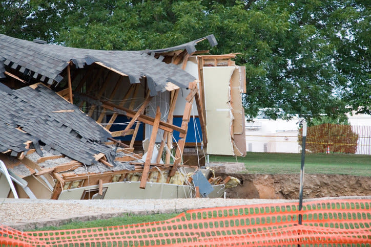 A collapsed house partially falling into a sinkhole