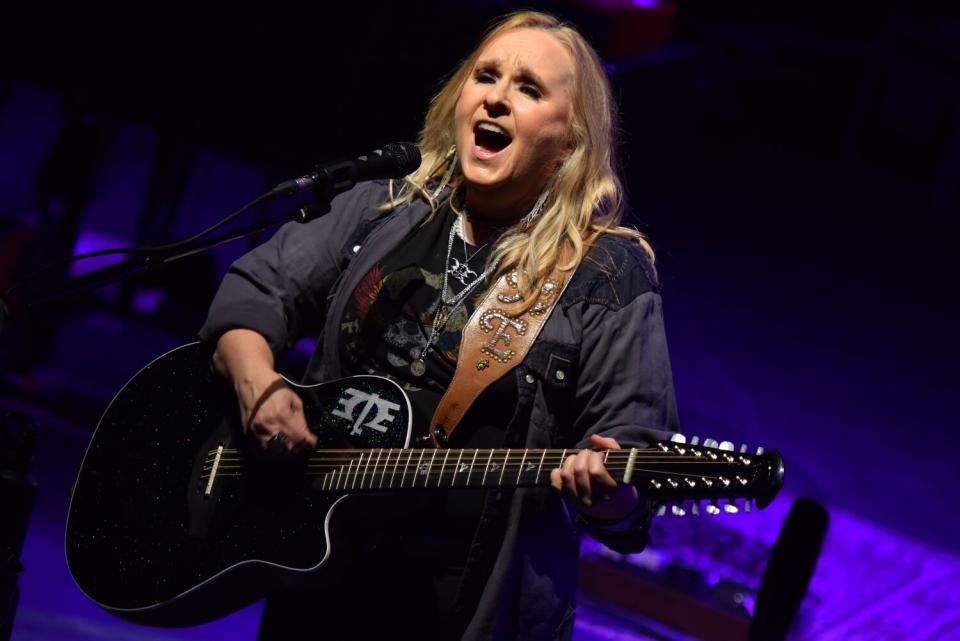 A woman sings and plays acoustic guitar onstage