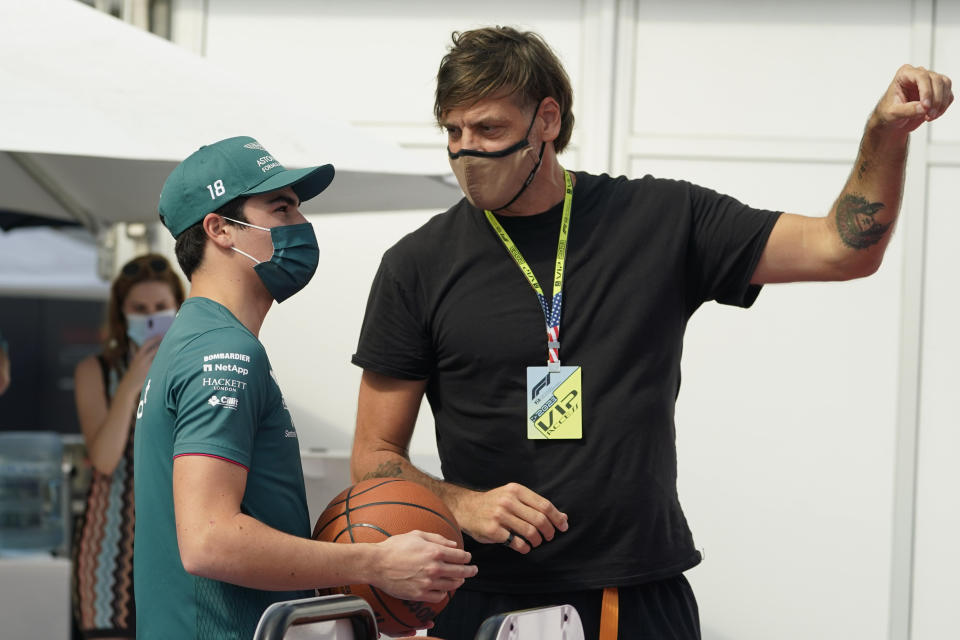 Aston Martin driver Lance Stroll of Canada, left, works with former NBA player Fabricio Oberto, right, at the Formula One U.S. Grand Prix auto race at the Circuit of the Americas, Thursday, Oct. 21, 2021, in Austin, Texas, as he practices before F1 Teams take part in a free throw challenge as they help the NBA celebrate their 75th Anniversary. (AP Photo/Eric Gay)