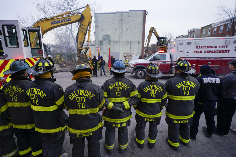 Firefighters stand in a line near an ambulance after a firefighter who died while battling a two-alarm fire in a vacant row home was pulled from the collapsed building, Monday, Jan. 24, 2022, in Baltimore. Officials said several firefighters died during the blaze. (AP Photo/Julio Cortez)