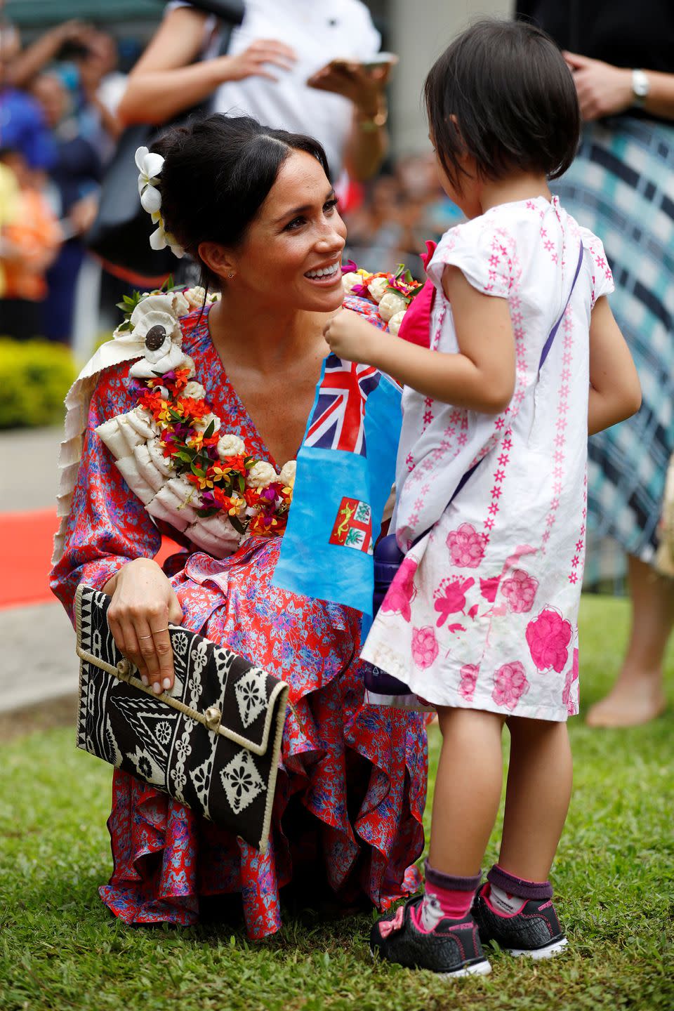 <p><strong>24 October </strong>The duchess knelt down to speak to a young girl. She carried a clutch bag that was made by local people<br>from the Suva Market. </p>