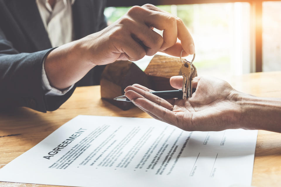 Estate agent giving house keys to customer and sign agreement in office.