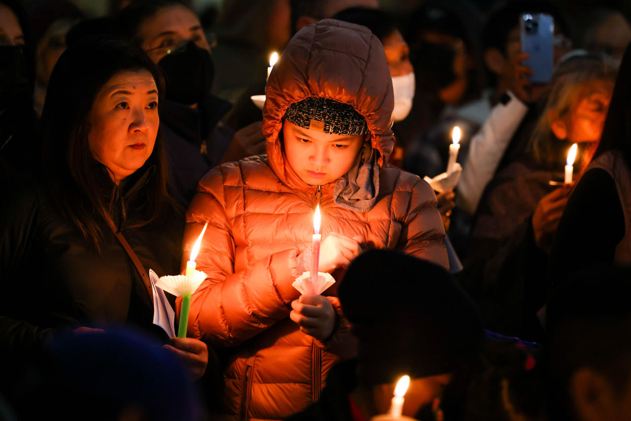 A girl in a hooded jacket, holding a candle, and an older woman, also with a candle, at a vigil in honor of the shooting victims.