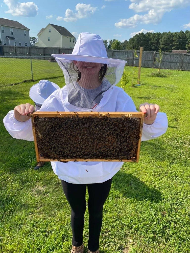 Taylor holds a honey frame in her bee suit, with her hands bravely bare.