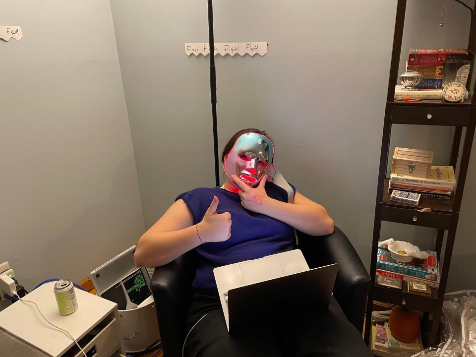 A person using an LED mask and a laptop.