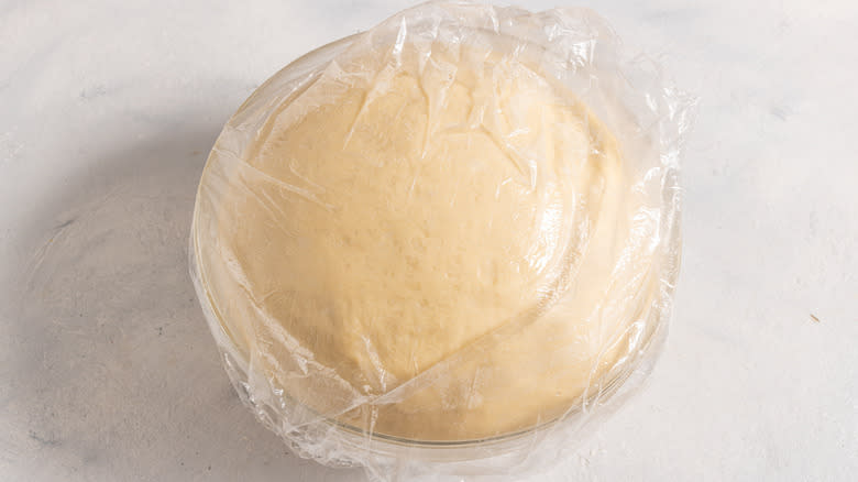 Risen dough inside a bowl covered with plastic wrap