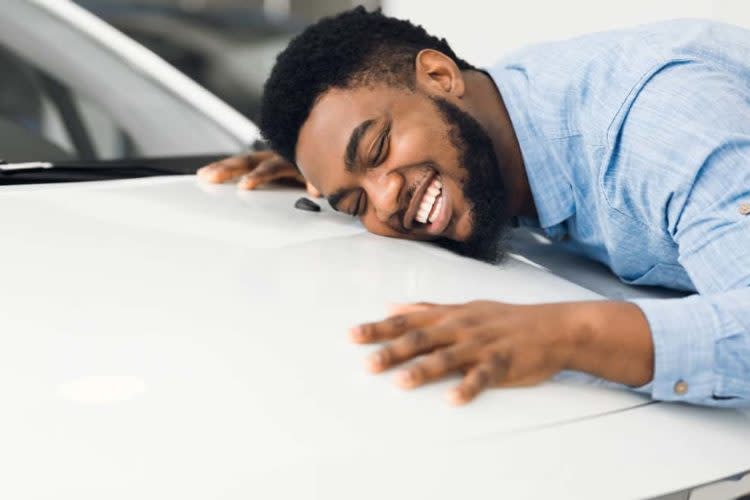 Happy African American Man Hugging New Car In Auto Dealership