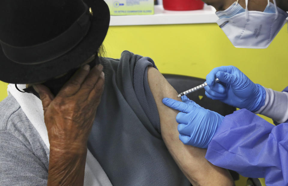 An elderly woman covers her face as she is inoculated with a dose of the Pfizer COVID-19 vaccine at the convention center converted into a vaccination site, in Quito, Ecuador, Wednesday, March 31, 2021. (AP Photo/Dolores Ochoa)
