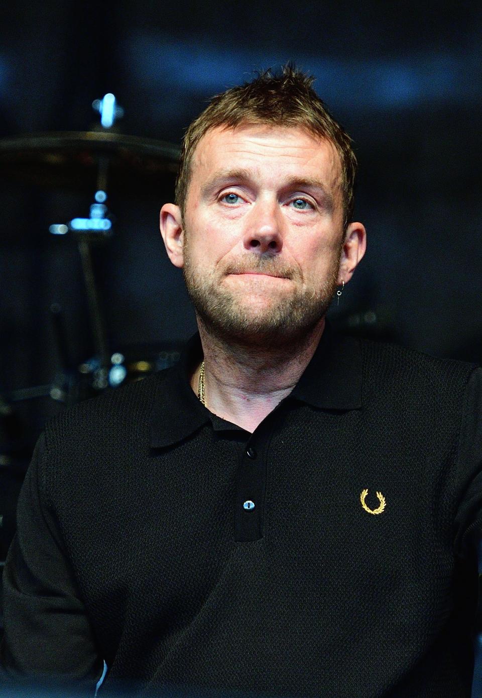Damon Albarn smiles while on stage, wearing all black