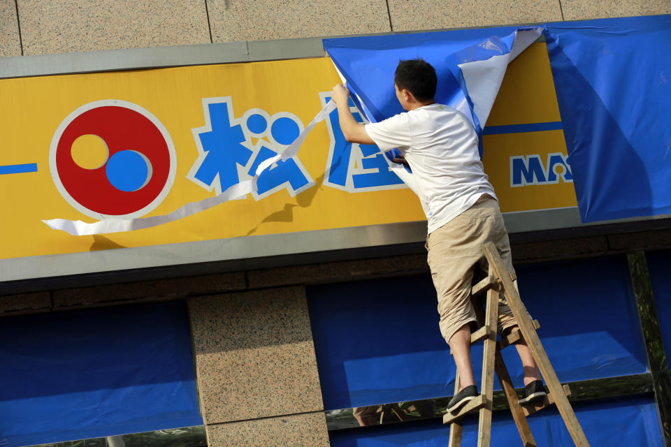 FILE - In this Monday, Sept. 17, 2012 file photo, A worker covers a signboard of a Japanese restaurant chain with blue sheets ahead of major protests expected on Tuesday, Sept. 18 near the Japanese Consulate General in Shanghai, China. Scores of Japanese-owned factories and stores in China were shuttered Tuesday as anti-Japanese demonstrations raged in dozens of cities. At stake are billions of dollars in investments and far more in sales and trade between Japan and China, the world's third- and second-largest economies. The two are so closely entwined, though, that both would suffer from any long-term disruptions. (AP Photo/Eugene Hoshiko, File)