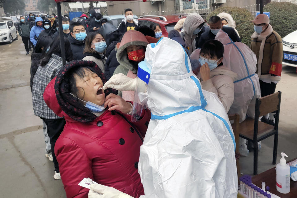 A medical worker wearing a protective suit takes swab samples for the COVID-19 test on residents in Huaxian county in central China's Henan province on Monday, Jan. 10, 2022. A third Chinese city has locked down its residents because of a COVID-19 outbreak, raising the number confined to their homes in China to about 20 million people. (Chinatopix via AP)