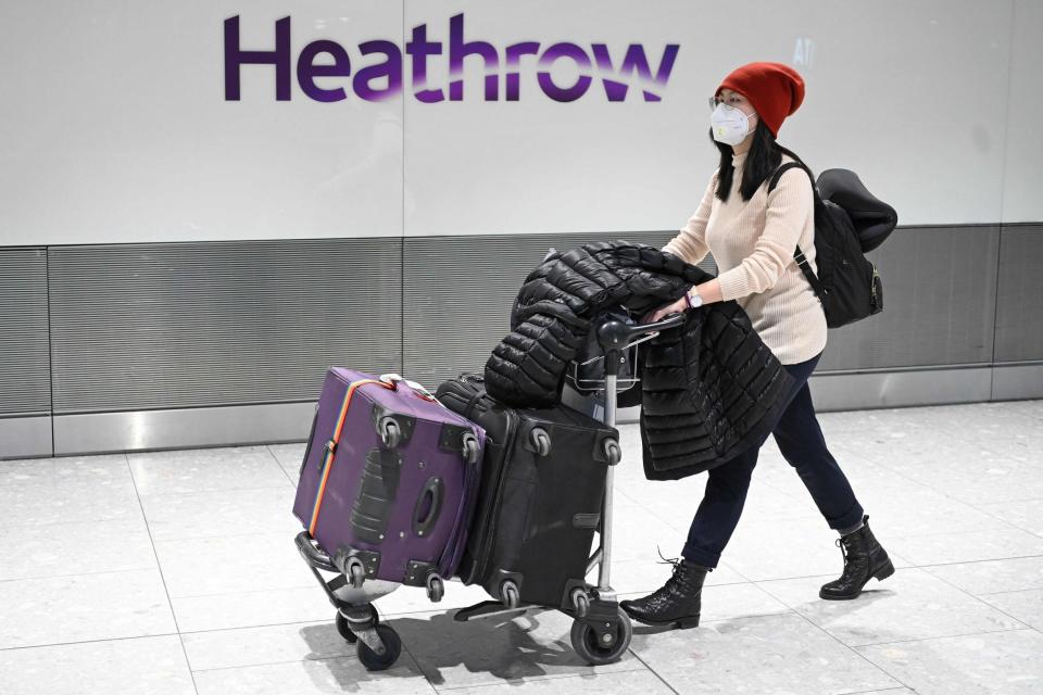 Passengers wear face masks as the push their luggage after arriving from a flight at Terminal 5 of London Heathrow Airport (AFP via Getty Images)
